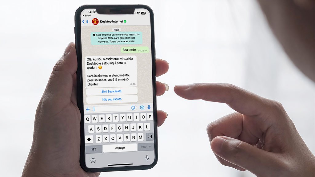 Uma pessoa segurando o celular com a mão esquerda. Na tela, uma conversa via WhatsApp da Desktop.