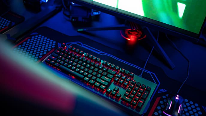 Uma mesa gamer com um teclado iluminado e parte de um monitor de computador com um jogo online.