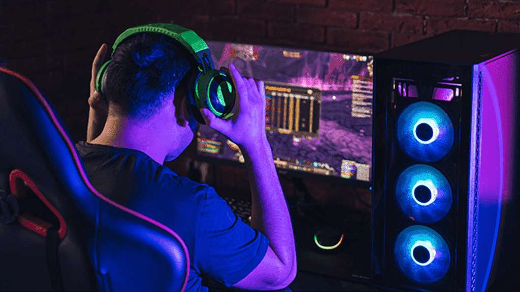 Um gamer com fone de ouvido, jogando no computador conectado à internet da Desktop. A imagem remete a um local escuro, com destaque para as luzes do jogo e do computador.