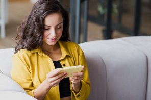 Uma mulher sentada no sofá lendo no celular. Ela usa o aplicativo do Skeelo.