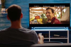 Um homem assistindo TV. Na tela do aparelho, uma cena do comercial da Desktop em que indica que a empresa oferece internet com o Wi-Fi 6.