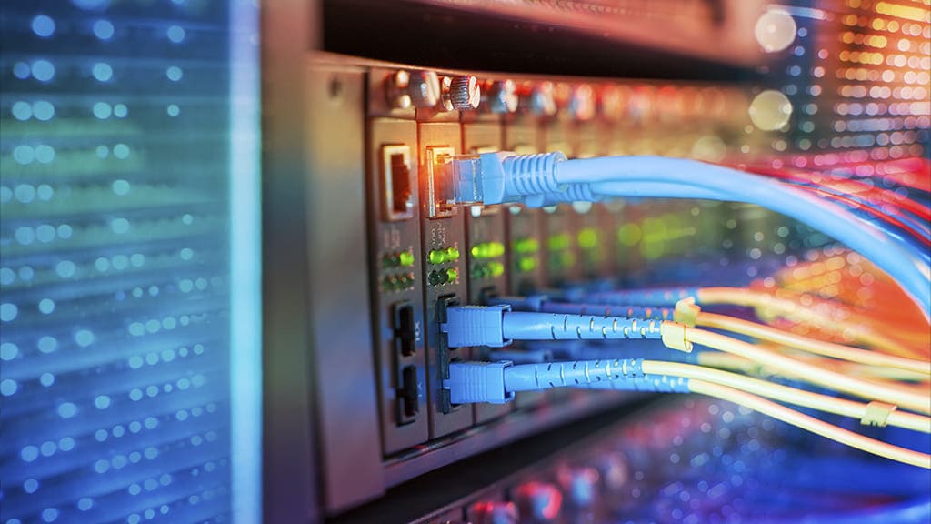 Um servidor de internet com várias entradas e cabos conectados. Ao fundo da imagem, várias luzes coloridas acessas.