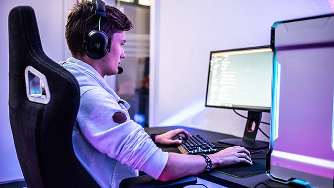Um gamer, sentado em uma cadeira gamer, à frente de um computador, jogando.