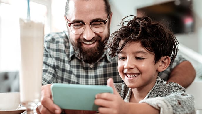 Um homem e uma criança sorrindo e segurando o celular. Eles jogam um jogo GaaS.