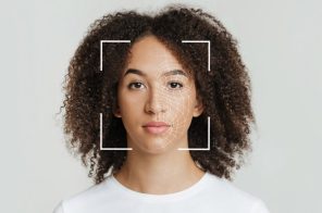 Na imagem, uma mulher negra, de cabelo solto até a altura dos ombros. Ela usa uma camiseta branca. O rosto dela está enquadrado em uma configuração de leitura de reconhecimento facial.