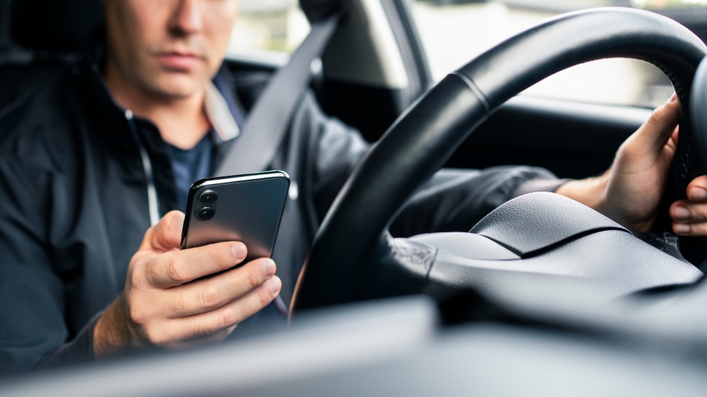 Um homem, dentro do carro estacionado, usando o celular