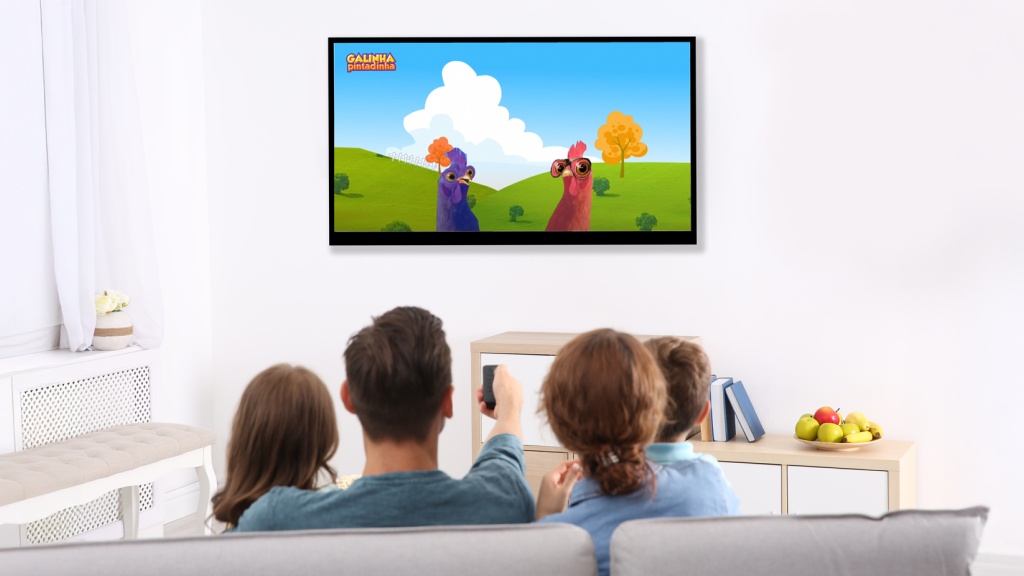 Família com pai, mãe e filhos sentados no sofá assistindo ao desenho Galinha Pintadinha, app disponível na Desktop