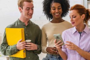 Homem jovem e duas mulheres em pé, enquanto uma segura o celular criando rede Wi-Fi para visitantes.