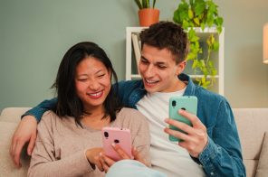Casal sorridente sentado no sofá, cada um segurando seu celular, representando a transferência de contatos de um celular para o outro.
