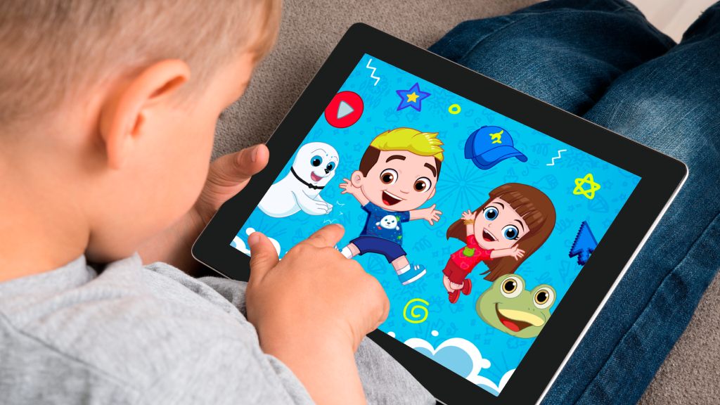 Menino vestindo camiseta cinza e calça jeans sentado no sofá assistindo aos conteúdos do Luccas Toon no tablet.