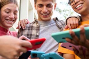 Grupo de amigos de pé na rua, sorridentes, compartilhando dados móveis entre si usando Android e iPhone.