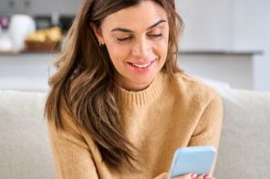Mulher de blusa amarela sorrindo no sofá, usando sua franquia de internet pelo celular.