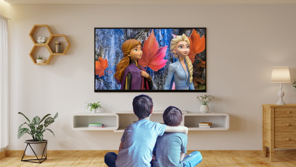 Dois meninos sentados no chão da sala, de pernas cruzadas e abraçados, assistindo ao filme Frozen no aplicativo infantil Disney+.