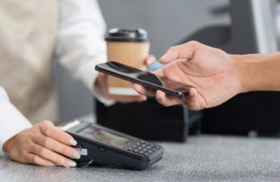 Pessoa realizando pagamento com NFC no celular aproximando o aparelho à maquininha.