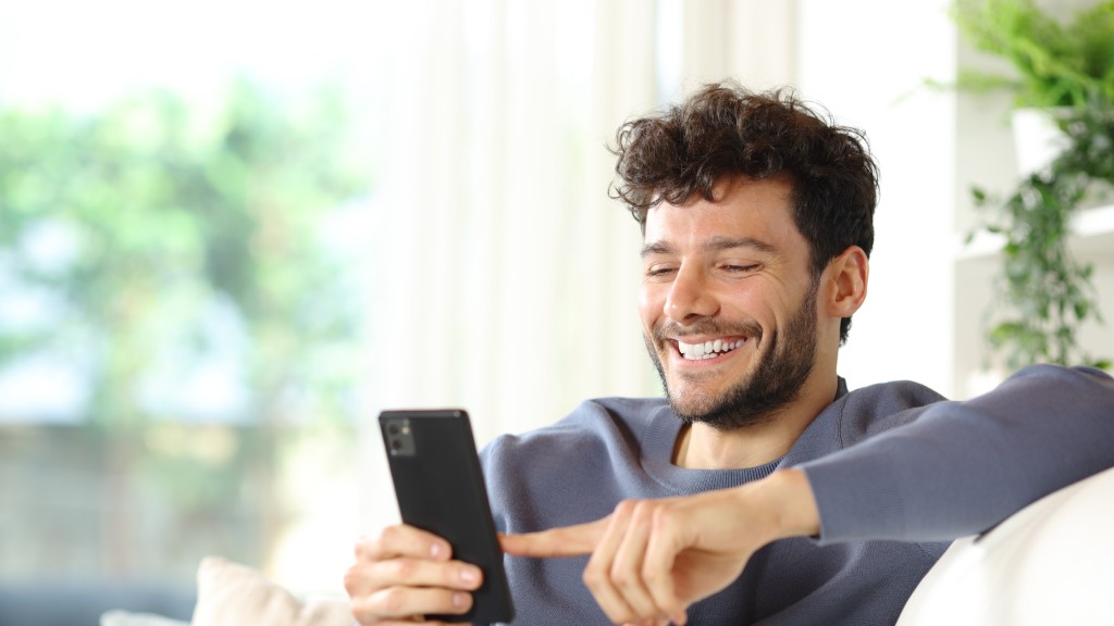 Homem jovem feliz com blusa moletom azul escuto navegando no celular conectado à rede Wi-Fi.