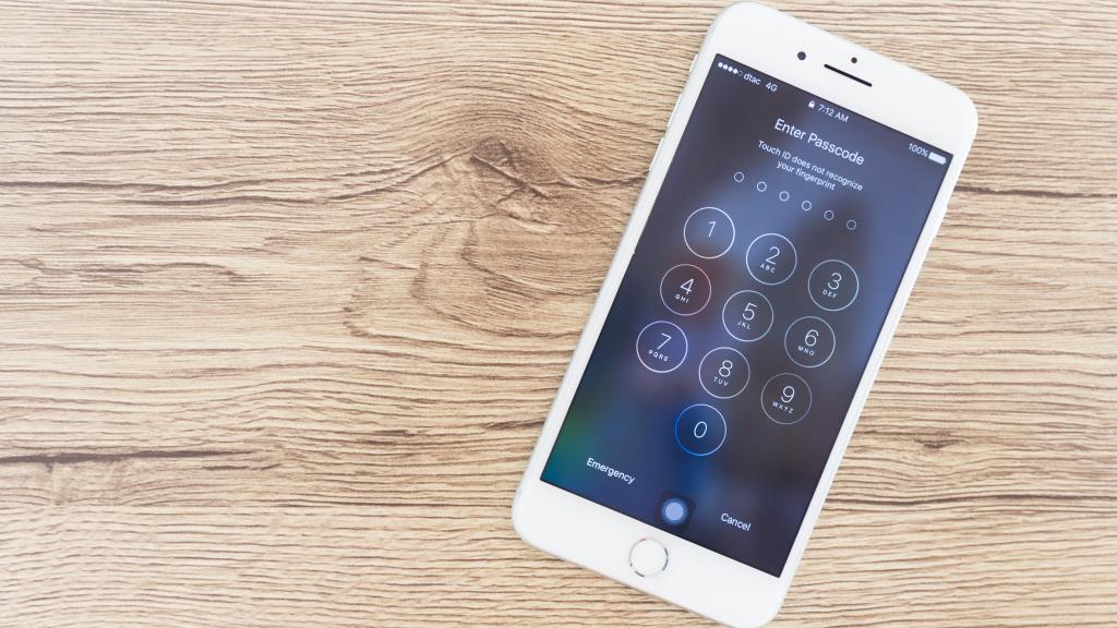 Celular iPhone branco em cima de uma mesa de madeira exibindo a tela de bloqueio.