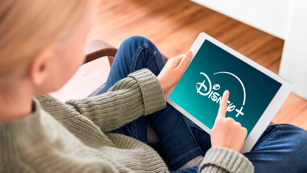 Criança sentada em cadeira com as pernas cruzadas enquanto navega no app do Disney+ no tablet.