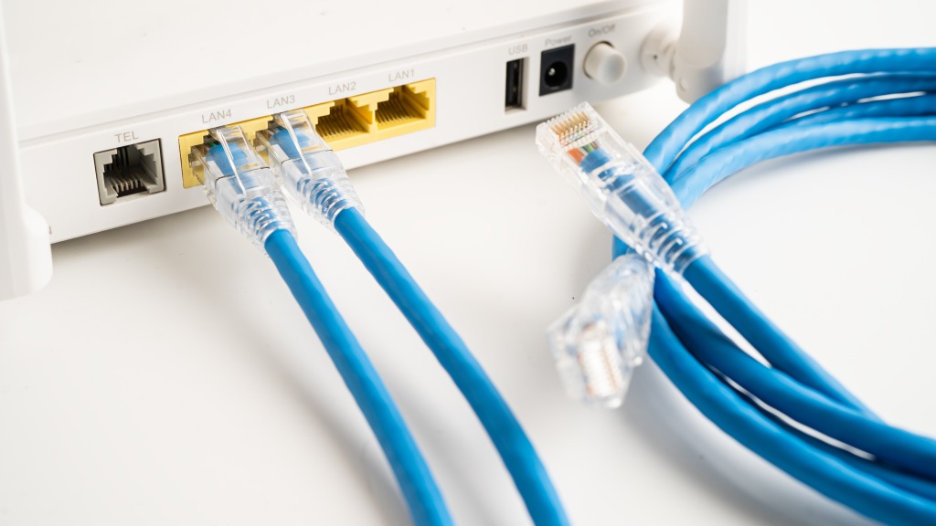 Parte traseira de um roteador branco com dois cabos conectados e um solto, enrolado, simbolizando tipos e diferenças entre os cabos de rede.