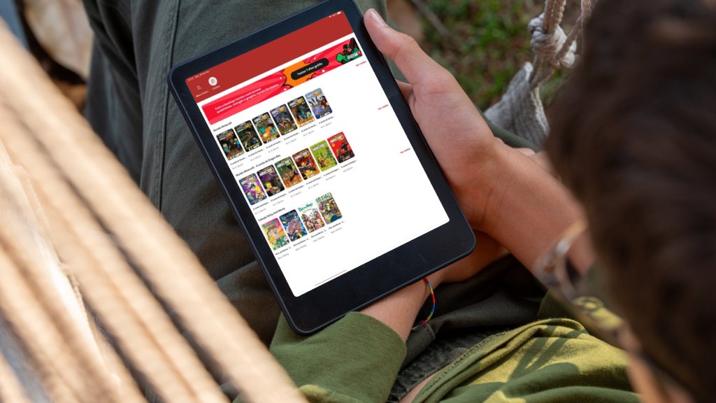 Homem sentado ao ar livre segurando um tablet que mostra a estante do app Desktop Comics, disponível nos planos da Desktop.