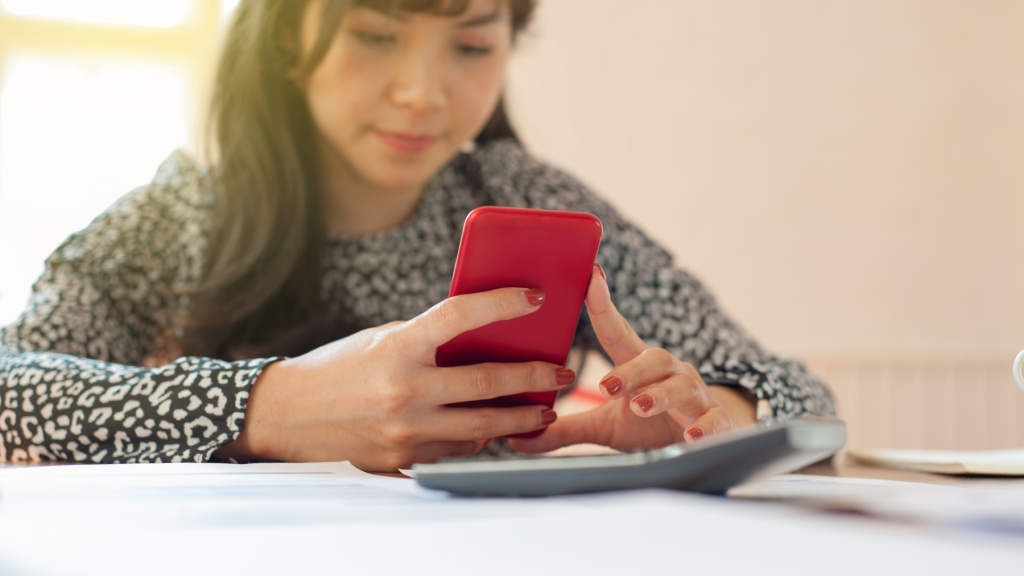Mulher jovem sentada à mesa segurando celular vermelho enquanto desliga a internet só do WhatsApp no Android.