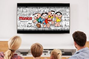 Pais com um menino e uma menina sentados em um sofá assistindo à Turma da Mônica na TV por meio do Monicaverso.