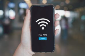 Mão segurando celular que exibe grande ícone de Wi-Fi branco, representando redes hotspot, com o texto 