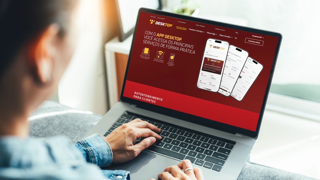 Uma pessoa segurando o notebook no colo. Na tela, a página da "Área do Cliente" do site da Desktop.