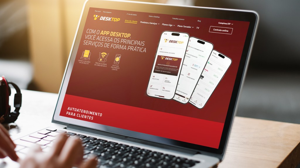 Mãos teclando em um notebook que exibe a Área do Cliente, um canal de atendimento da Desktop.
