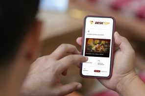 Um homem segurando o celular, na tela do aparelho, a página inicial do aplicativo da Desktop