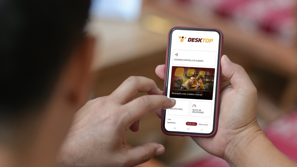 Um homem segurando o celular, na tela do aparelho, a página inicial do aplicativo da Desktop