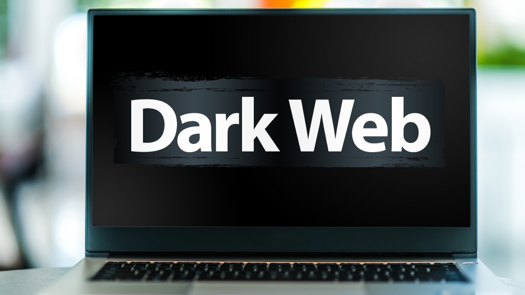 Notebook sobre uma mesa exibindo, na tela, o texto 'Dark web' em branco sobre fundo preto.