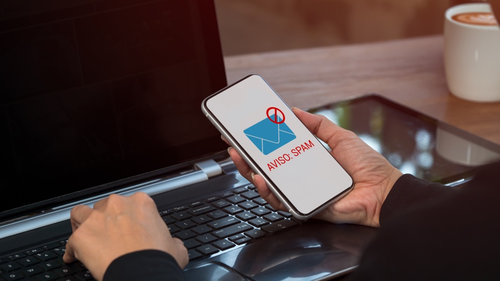 Mão segurando celular com ícone de caixa de entrada e texto indicando "Aviso: spam", ilustrando o que é spam e seus principais tipos.