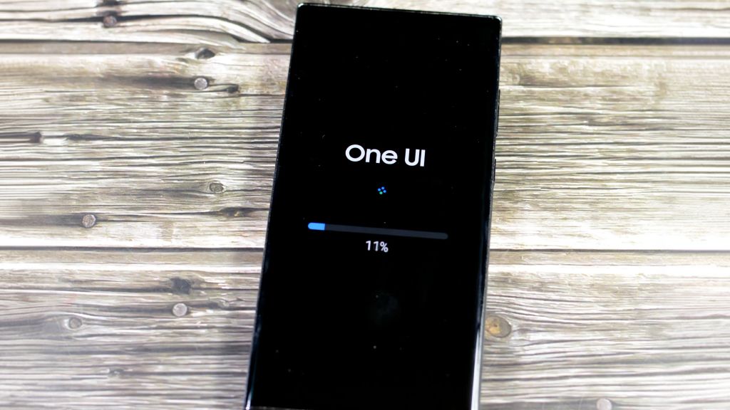 Celular Android sobre uma mesa de madeira exibindo na tela o status de reinicialização após uma atualização, com barra de progresso em 11%.