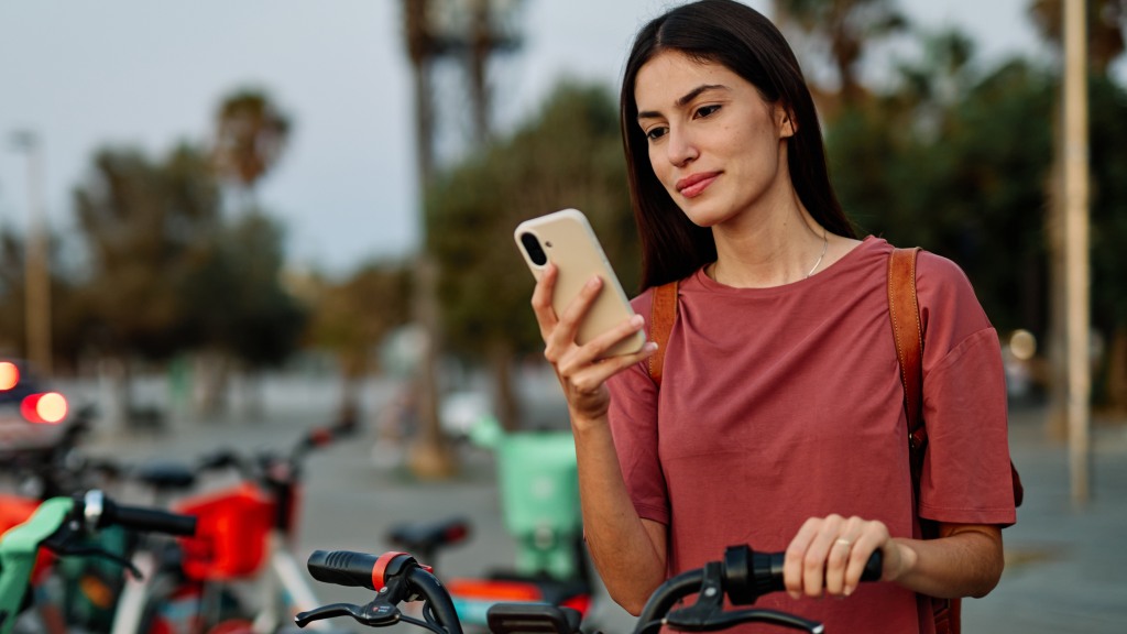 Mulher jovem com camiseta vermelha ao ar livre, com uma das mãos no guidão da bicicleta e a outra segurando um celular conectado ao plano controle da Desktop.