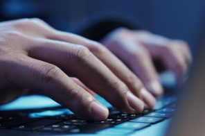 Mãos de uma pessoa anônima digitando em um notebook, com iluminação azul ao fundo, representando a dúvida sobre a diferença entre deep web e dark web.