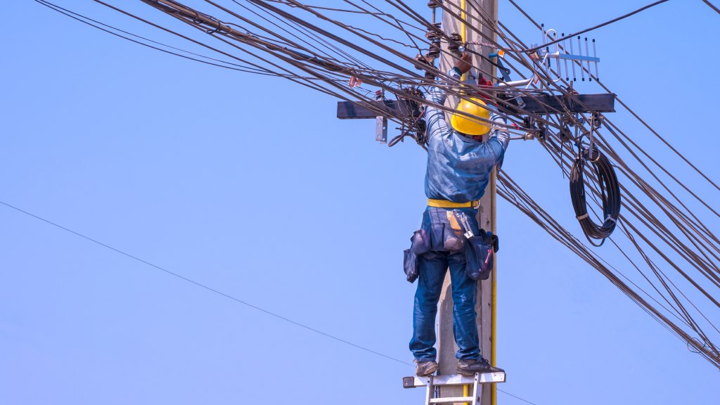 Técnico de internet no poste instalando o cabeamento de internet fibra óptica, tornando o serviço disponível no endereço.