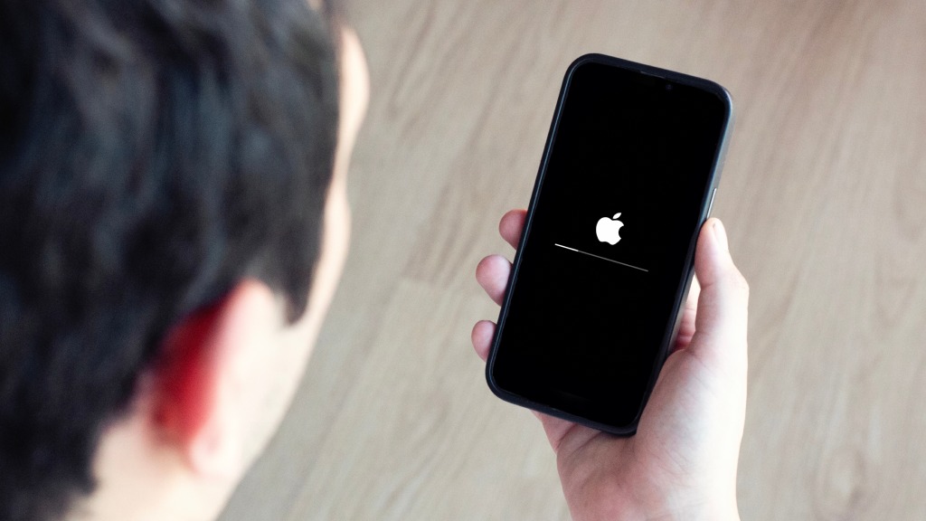 Homem visto de trás, desfocado, segurando um iPhone que exibe na tela o status de reinicialização após atualização, com o logo da Apple.