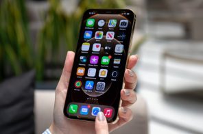 Mãos segurando celular iPhone, que exibe a Tela de Início do iPhone, representando a dúvida de como desativar aplicativos em segundo plano no aparelho.