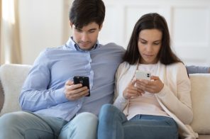 Casal sentado no sofá, ambos olhando para o celular enquanto compartilham internet entre os aparelhos.