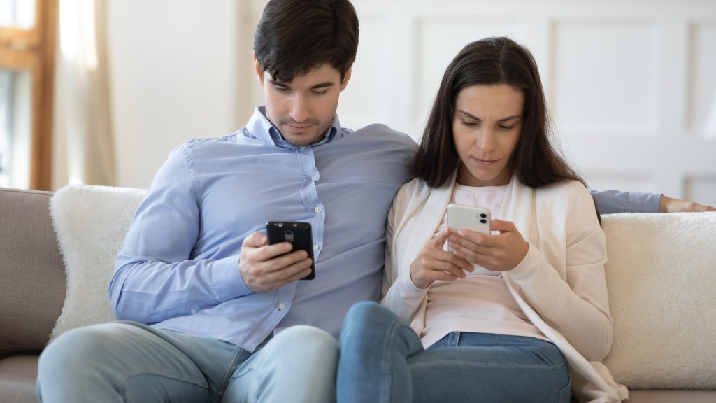 Casal sentado no sofá, ambos olhando para o celular enquanto compartilham internet entre os aparelhos.