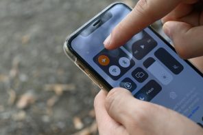 Mãos segurando um iPhone com a Central de Controle aberta, enquanto o dedo indicador aponta para o ícone do modo avião ativado.