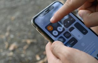 Mãos segurando um iPhone com a Central de Controle aberta, enquanto o dedo indicador aponta para o ícone do modo avião ativado.