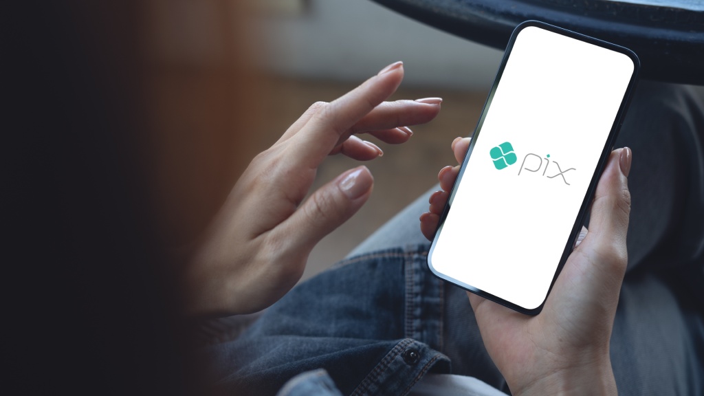Mãos segurando celular, que exibe o ícone do Pix na tela, representando o recurso "Pix automático".