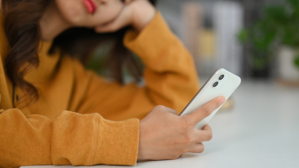 Moça com blusa amarela debruçada sobre a mesa, com uma das mãos na cabeça, demonstrando decepção ao navegar no aparelho por problemas de internet.