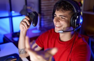 Rapaz gamer com camiseta vermelha, headphones pretos e controle de videogame na mão direita, sorrindo durante a partida após monitorar quantos Mega tem sua internet.
