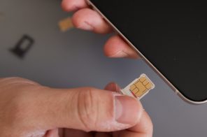 Mão segurando celular com uma mão e microchip com a outra, simbolizando a portabilidade de chip para a troca de operadora sem mudar o número.