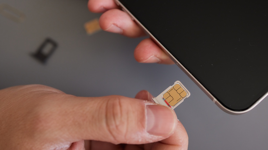 Mão segurando celular com uma mão e microchip com a outra, simbolizando a portabilidade de chip para a troca de operadora sem mudar o número.