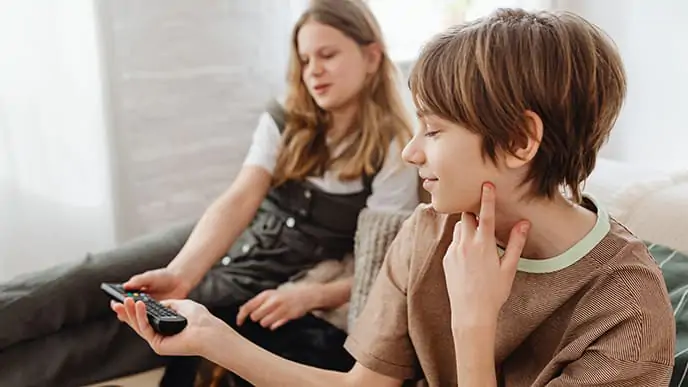 Os canais infantis são uma ótima opção para o entretenimento de crianças de todas as idades. Duas crianças, um menino e uma menina, sentadas no sofá. O menino segura o controle da televisão.