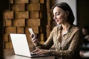 Uma mulher usando o notebook e segurando um celular